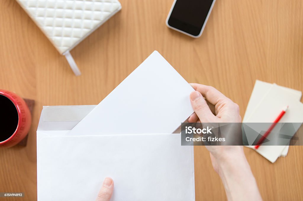 Female hands holding an envelope with a sheet over office Female hands holding an envelope with a blank paper sheet over the office desk. Top view with copy space Envelope Stock Photo