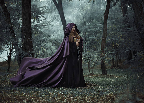 Wicked witch in a long dark cloak wandering in woods On the eve of Halloween witch casts a spell, decided to collect a potion to brew, walking in the mysterious woods, keeping his book with conspiracies. Fabulous and mystical concept. Fashionable toning. Creative color. wizard photos stock pictures, royalty-free photos & images