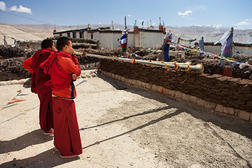 Young Tibetan monks playing buddhist horns on the roof of monastery in Lo Manthang. Mustang region is the former Kingdom of Lo and now part of Nepal,  in the north-central part of that country, bordering the People's Republic of China on the Tibetan plateau between the Nepalese provinces of Dolpo and Manang. The Kingdom of Lo, the traditional Mustang region, and “Upper Mustang” are one and the same, comprising the northern two-thirds of the present-day Nepalese Mustang District, and are well marked by official “Mustang” border signs just north of Kagbeni where a police post checks permits for non-Nepalese seeking to enter the region, and at Gyu La (pass) east of Kagbeni.http://bhphoto.pl/IS/mustang_380.jpg