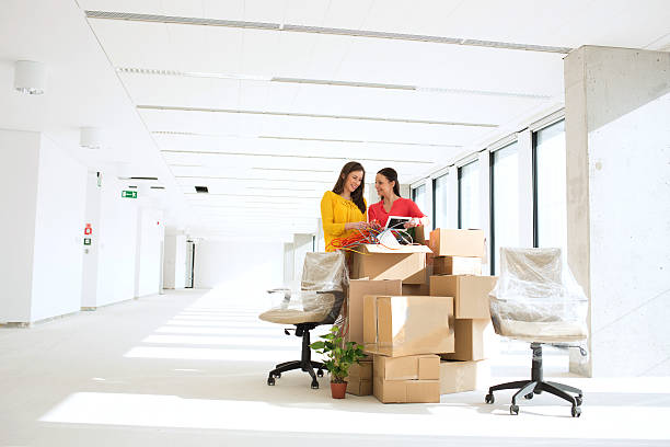 Businesswomen unpacking cardboard boxes in new office stock photo