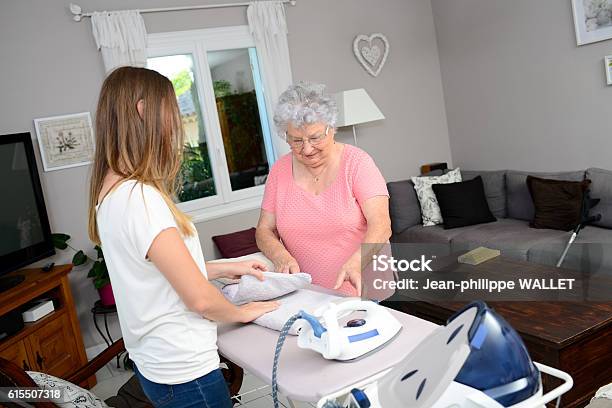 Cheerful Young Girl Ironing And Helping Elderly Woman At Home Stock Photo - Download Image Now