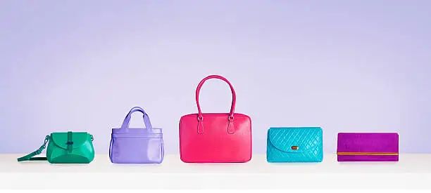 Photo of Colorful bags and purses isolated on purple background with copyspace.