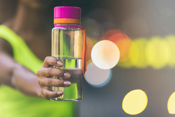 Young woman of african descent jogging in the city at night, holding a bottle of water