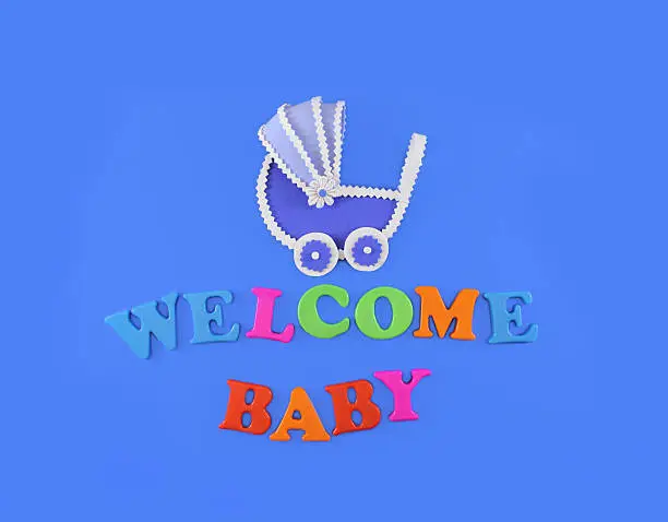 Baby carriage on light blue background, with text Welcome Baby. Baby shower concept in flat lay