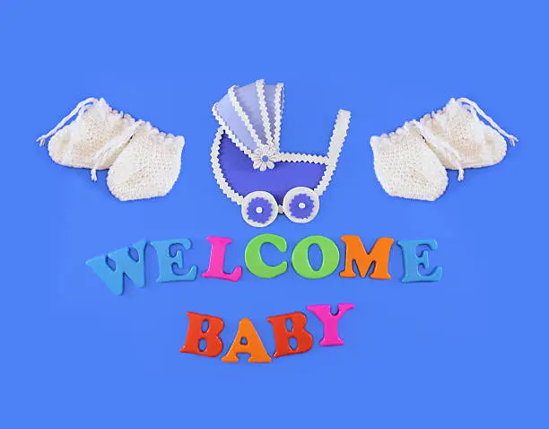 Baby carriage and baby shoes on light blue background, with text Welcome Baby. Baby shower concept in flat lay