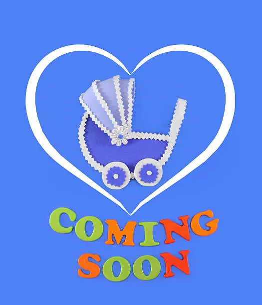 Baby carriage inside a white heart, with text Coming Soon. Baby shower concept in flat lay