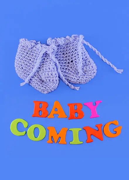 Hand-knit Organic Wool Baby shoes. Baby shower concept in flat lay, with text Baby Coming