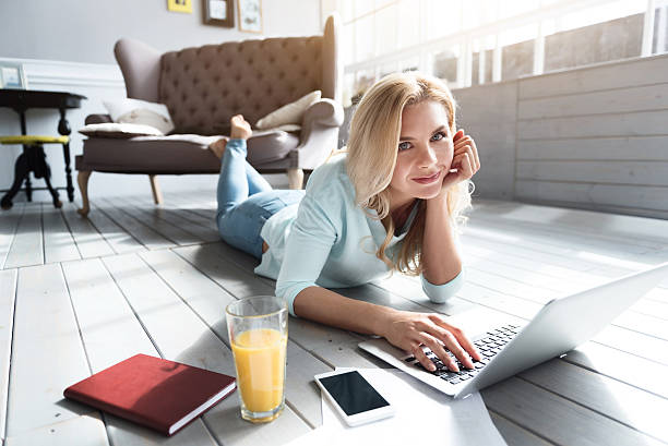 istock Blond woman lying on floor and using laptop 615518962