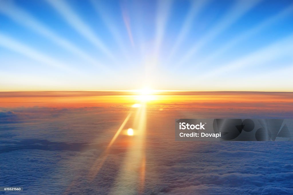 Sun, sunset, blue sky, and ocean of clouds View on orange sunset, sun, blue sky, and ocean of clouds from airplane window. Planet Earth Stock Photo