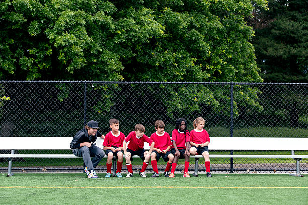 Coach talking to his co-ed diverse soccer team sitting on the bench