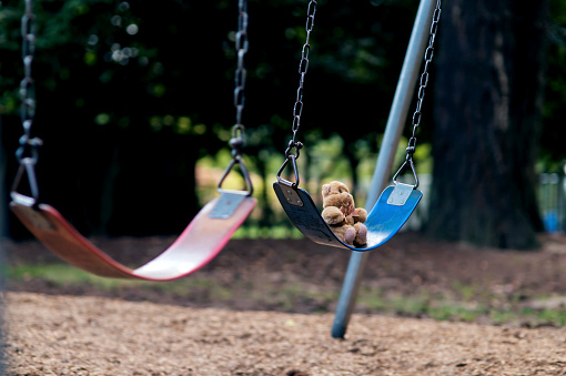 Teddybear sitting alone on a swingset at a local park