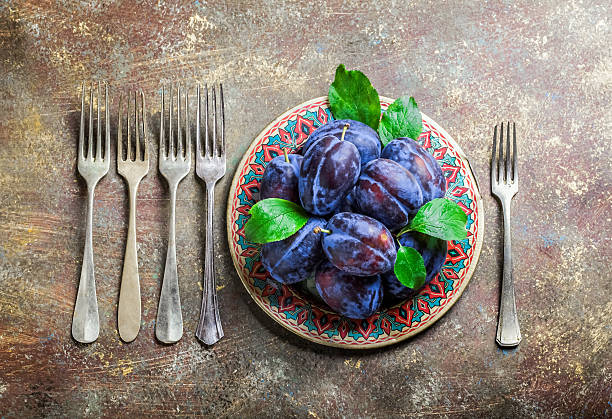 istock Plums overhead group with forks on plate and painted background 615523070