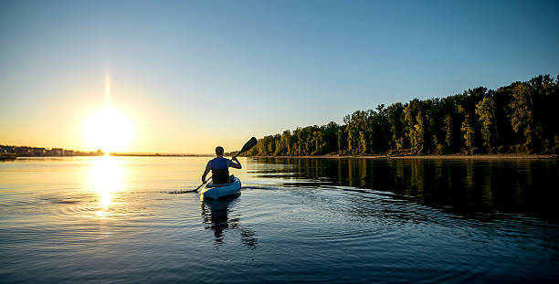 un homme adulte pagayant en kayak sur une rivière au coucher du soleil - kayaking photos et images de collection
