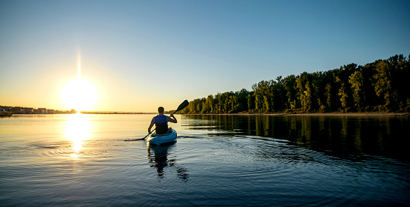 Adult male paddling a kayak on a river at sunset