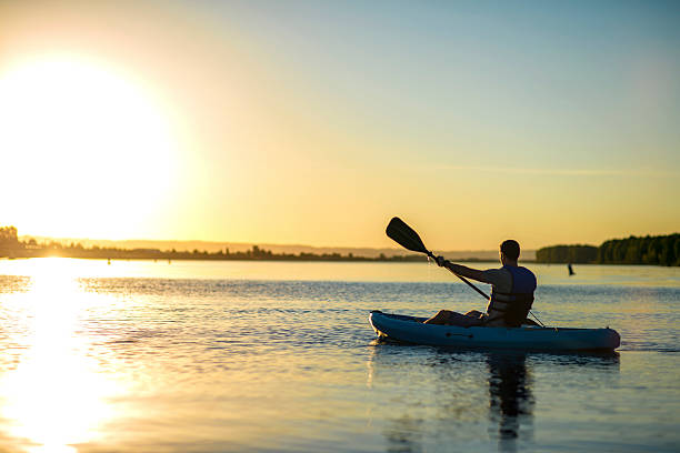 istock Male paddling a kayak on water as the sun sets 615523170