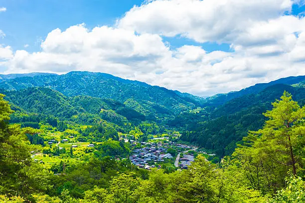 A view overlooking Tsumago village above the Magome-Tsumago portion of ancient Nakasendo Route from high angle viewpoint and former grounds of Tsumago castle in Japan on a blue sky day. Horizontal
