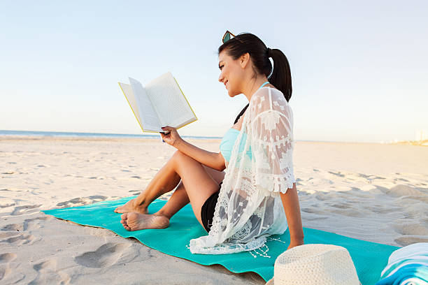 istock Beautiful woman reads a book on the beach 615610604