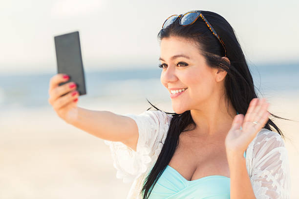 istock Beautiful woman waves while taking selfie at the beach 615610616