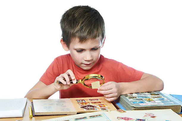 Boy with magnifying glass looks his stamp collection isolated white