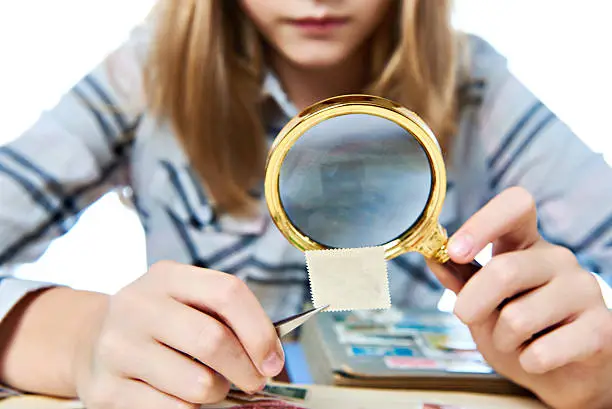 Teen girl with magnifying glass looks his stamp collection