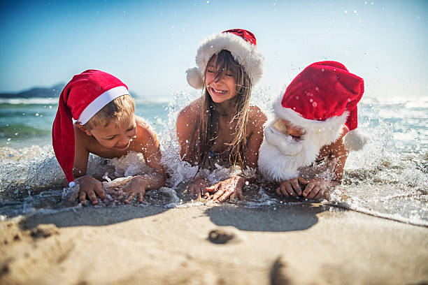Kids having fun on the beach during Christmas It's christmas on the beach. Kids wearing santa hats having fun on beach - laughing and screaming in water. girls laying on beach stock pictures, royalty-free photos & images