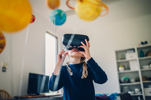 Little girl at home on her own. She is wearing a virtual reality headset with some homemade planets partly seen in the image. Focus on the little girl. View from below