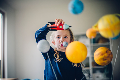 Little girl playing with her homemade planetarium as she holds an astronaut and spacecraft. Arms raised as she flies them over the planets.