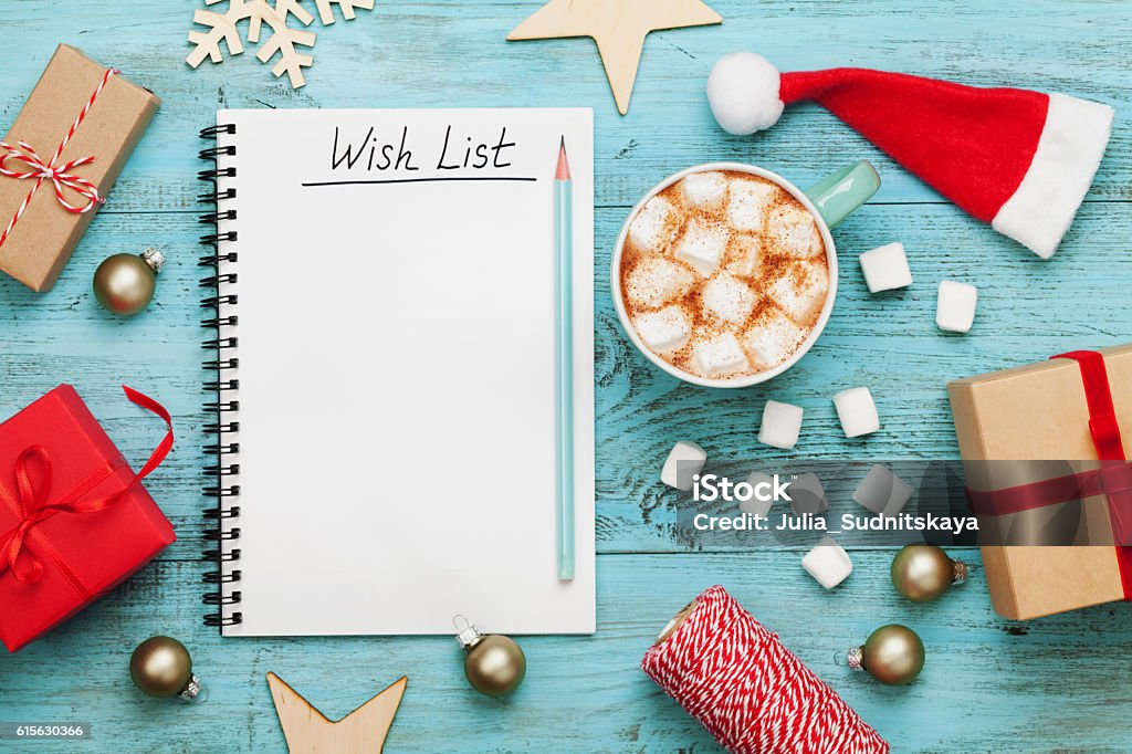 Cocoa or chocolate, holiday decorations and notebook, christmas planning concept. Cup of hot cocoa or chocolate with marshmallow, holiday decorations and notebook with wish list on turquoise vintage table from above, christmas planning concept. Flat lay style. Wish List Stock Photo
