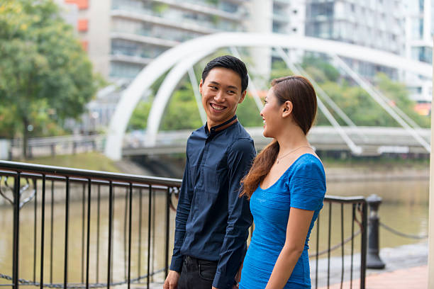 istock Young Asian Couple Scrolling in City Park 615633800