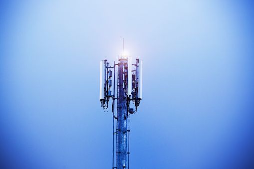 The top of an illuminated mobile phone tower  rises into the evening's indigo sky.