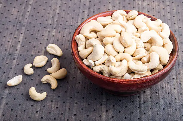 Selective focus on at the tasty and healthy raw cashew nuts in a brown bowl on fabric background