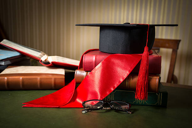 istock Graduation cap and red ribbon lying on books at library 615638922