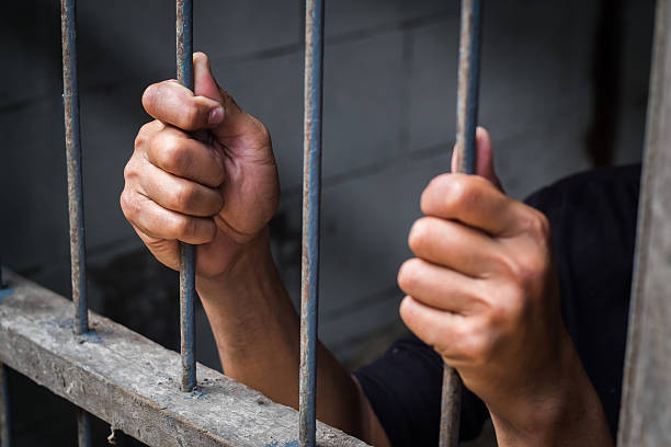 istock Hands of man behind jail bars. 615639548