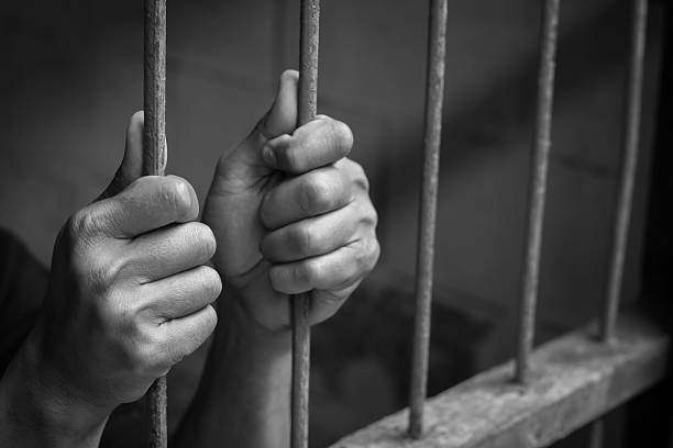 istock Hands of man behind jail bars. 615639650