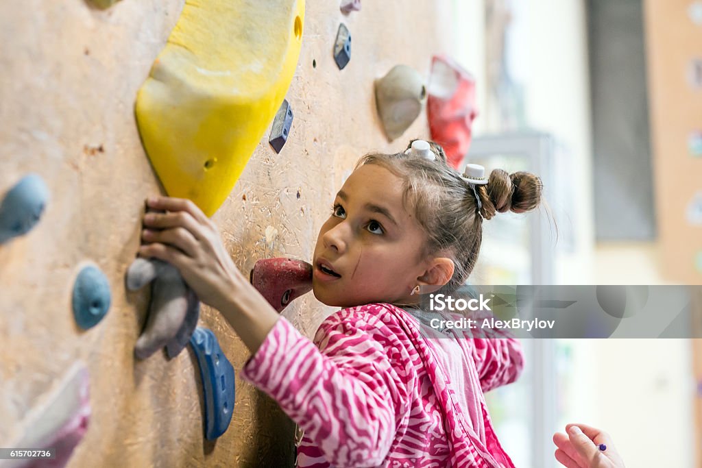 Junior Climber hanging on holds on climbing wall Junior Climber Girl shirt hanging on holds on climbing wall of indoor gym Child Stock Photo