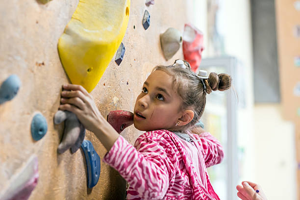 Junior Climber hanging on holds on climbing wall Junior Climber Girl shirt hanging on holds on climbing wall of indoor gym rock climbing stock pictures, royalty-free photos & images