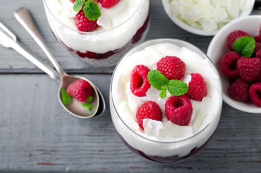 Healthy breakfast, desert, with chia seed pudding, cream, raspberry jam, coconut flakes and fresh berries, on wooden background