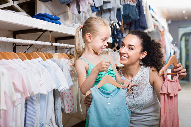 Woman with small daughter choosing clothes Young cheerful woman with small daughter choosing clothes in kids apparel boutique baby boutique stock pictures, royalty-free photos & images