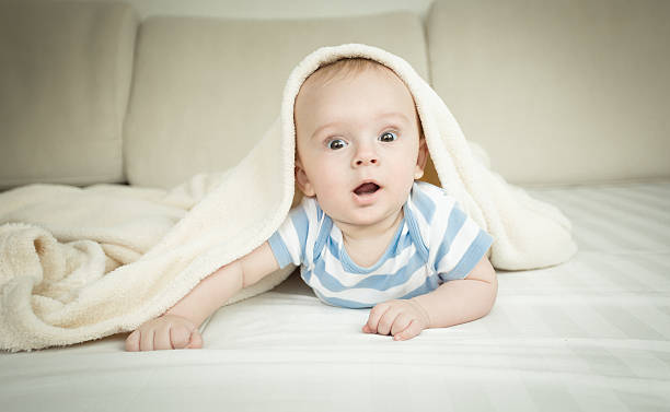 istock Surprised baby boy looking at camera from under the blanket 615704718