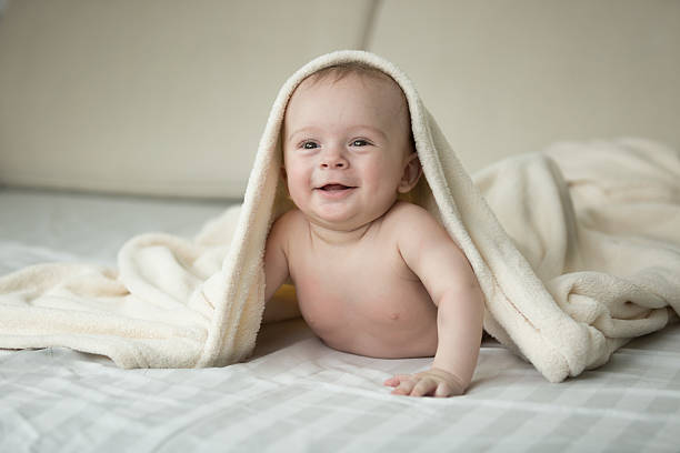 istock Cute laughing baby lying under blanket on bed 615705638