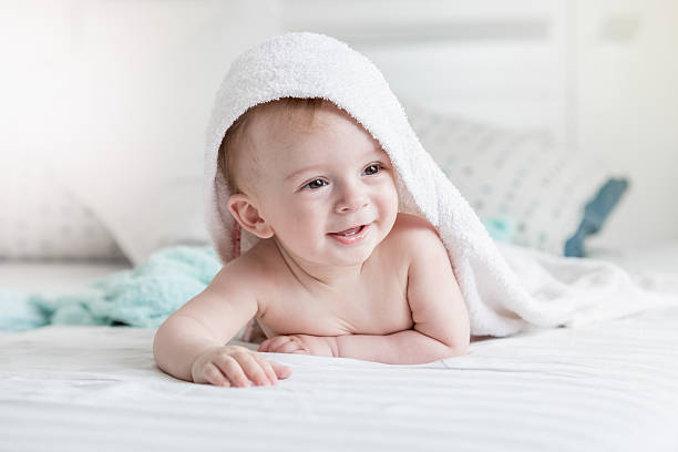 istock Smiling baby in towel ling on bed after having bath 615706922