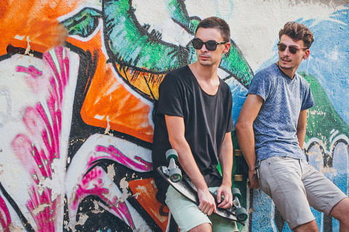 Rebel teenagers standing against brick wall and holding skateboards in their hands.