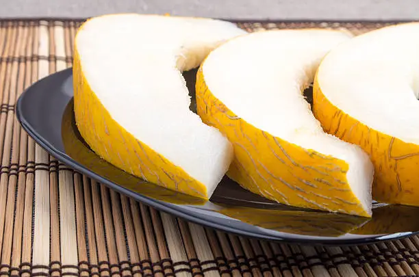 Three slices of juicy yellow melon on a black plate closeup on wooden background