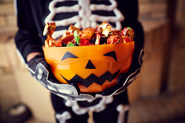 junge im skelett kostüm halten schale voller süßigkeiten - halloween stock-fotos und bilder