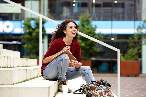 istock Attractive young woman sitting on steps with notebook and smiling 615729866
