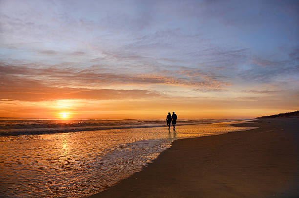 istock Senior couple holding hands walking on beach enjoying sunrise. 615730904