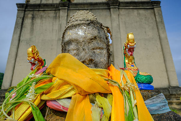 istock Public ancient head Buddha statue left in the forest 615731080