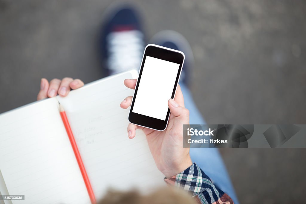 Hand holding a smartphone against a copybook with a pencil Hand holding a smartphone against an open copybook with a pencil and messaging. Back to school concept photo, vertical, view over the head Telephone Stock Photo