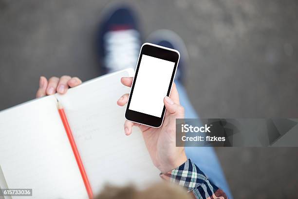 Hand Holding A Smartphone Against A Copybook With A Pencil Stock Photo - Download Image Now