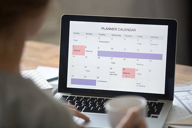 Open laptop on the desk, planner calendar on the screen Open laptop on the desk with a planner calendar on the screen. Education concept photo, view over the shoulder, close up busy calendar stock pictures, royalty-free photos & images